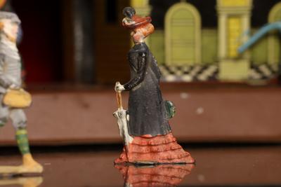 Figurilla de plomo: mujer con vestido negro y rojo.